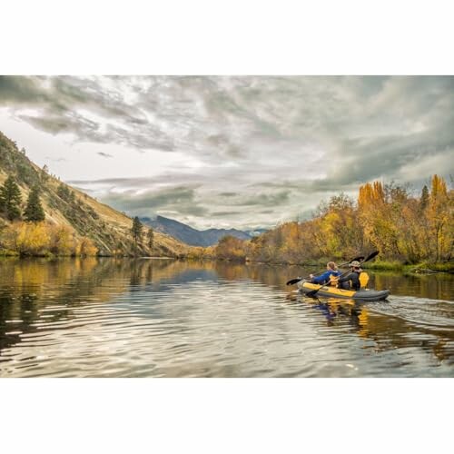 Two people kayaking on a calm river surrounded by autumn foliage under a cloudy sky.