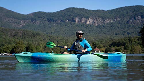 Man kayaking on a lake with mountains in the background.