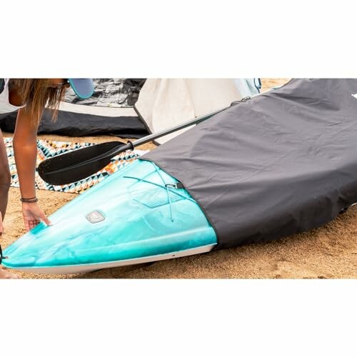 Person covering a paddleboard with a protective cover on the beach.