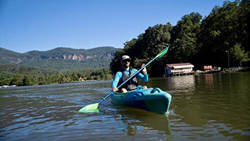 Person kayaking on a lake with mountains in the background.