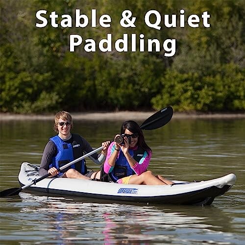 Two people kayaking on calm water with trees in the background.