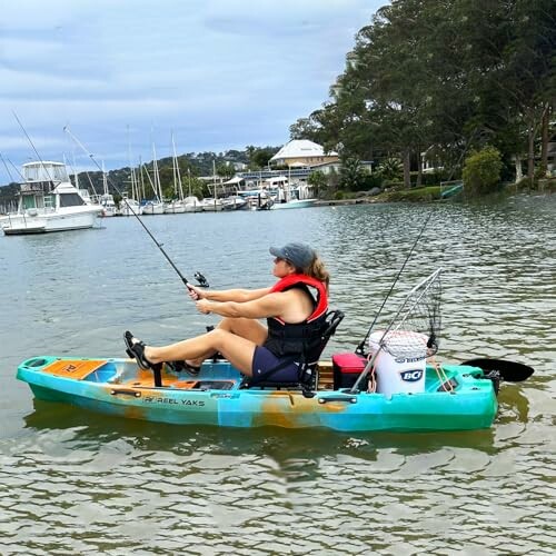 Woman fishing from a kayak on a river with boats in the background.